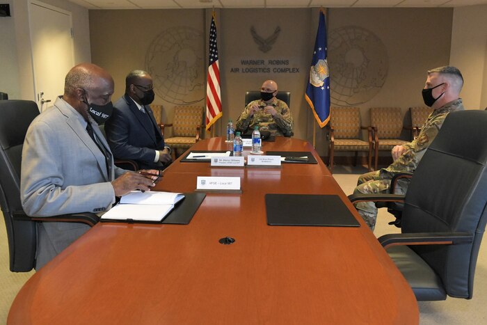 Photo shows four men seated at a conference table.