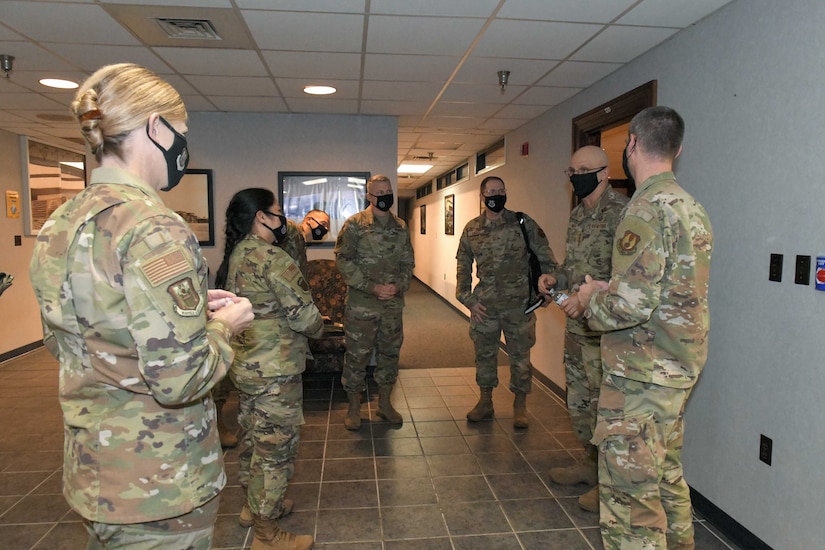 Photo shows a group of people standing in a hallway talking.