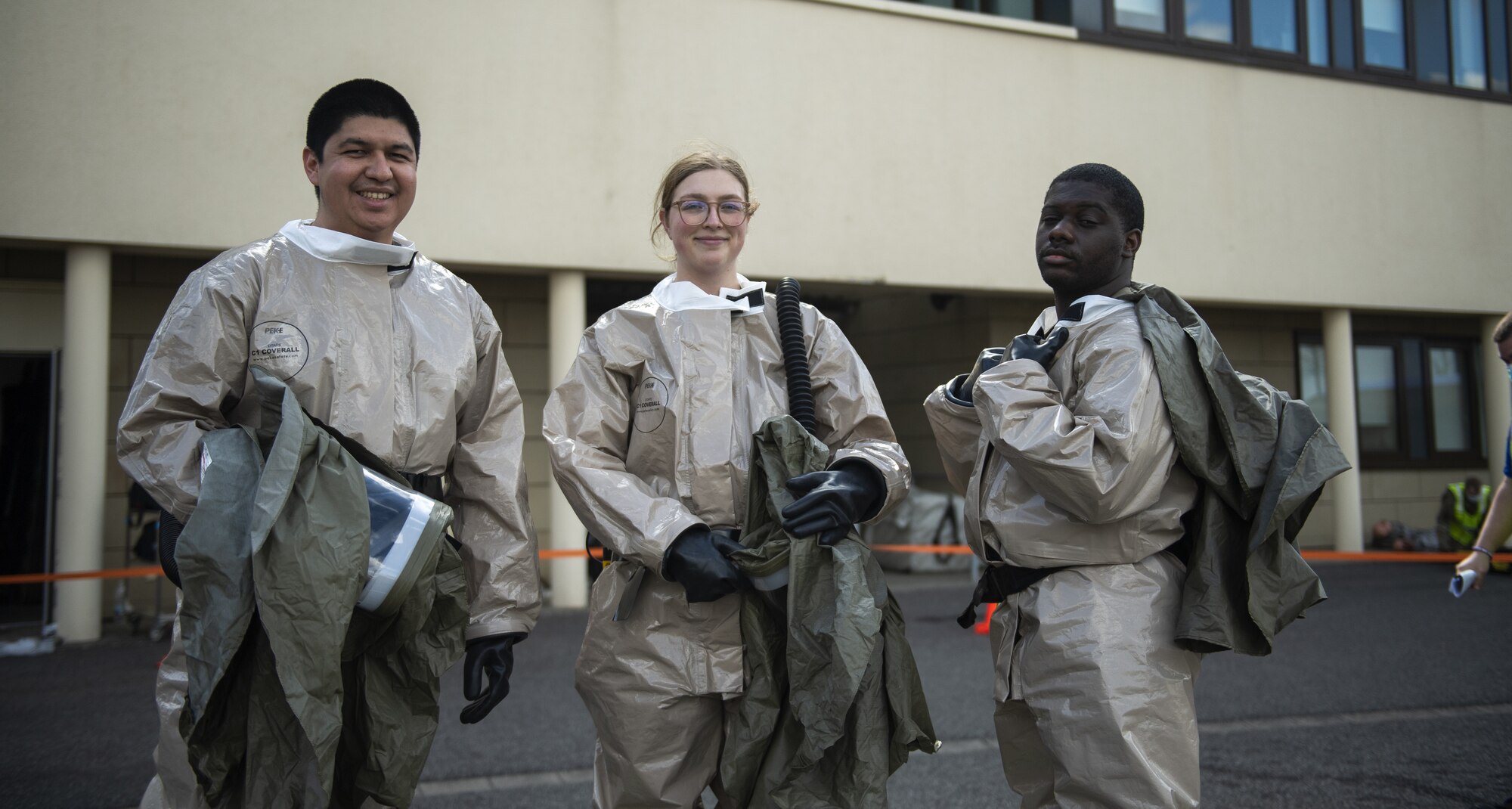 Three U.S. Air Force Airmen from the 52nd Medical Group Airmen pose for a photo near a decontamination site pop-up behind the Medical Group building at Spangdahlem Air Base, Germany, March 26, 2021. After the initial disaster simulation at the base theater, patients were transported to the decontamination site where Medical Group Airmen awaited their arrival and performed simulated decontamination procedures. (U.S. Air Force photo by Senior Airman Ali Stewart)
