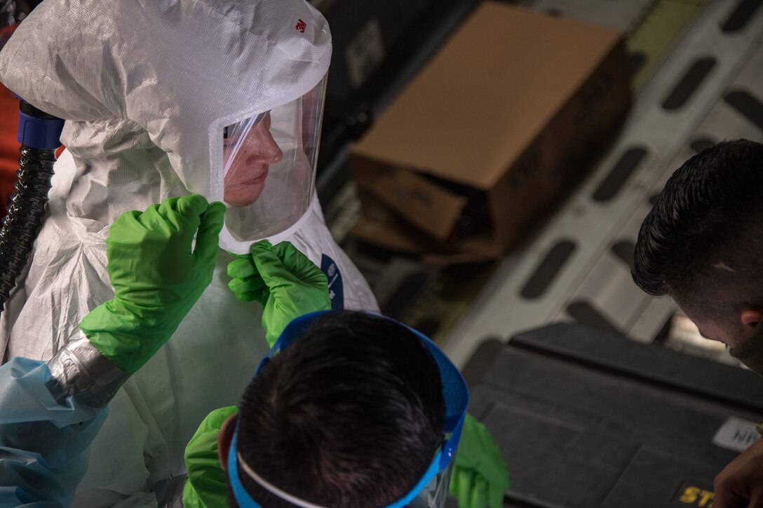 An airman assists another airman seal their personal protective equipment