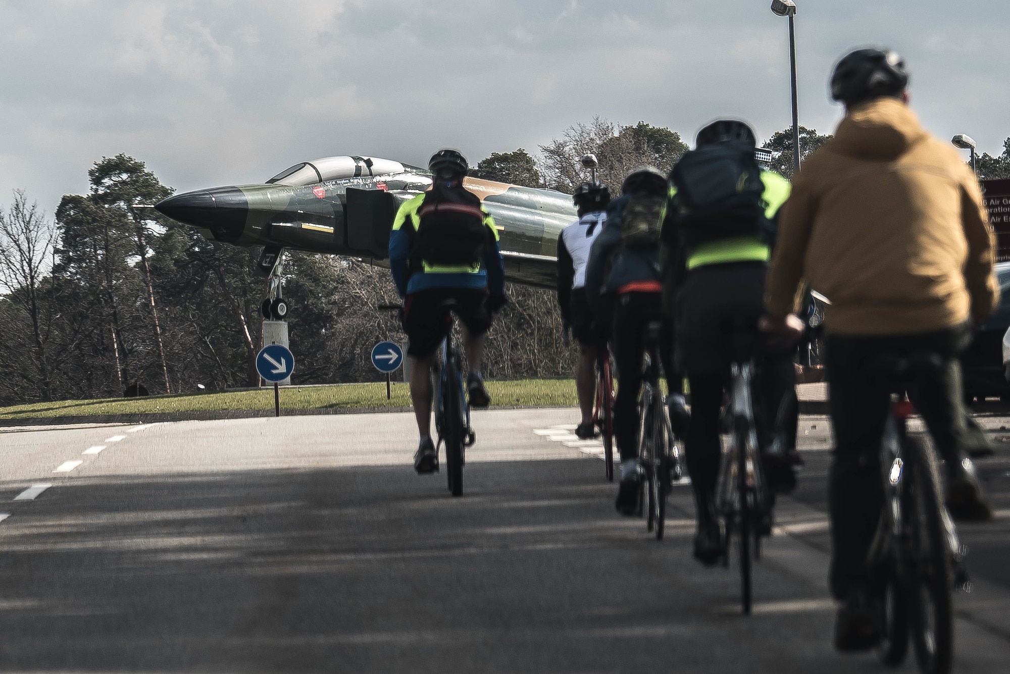 Several people ride their bicycles toward an aircraft static display.