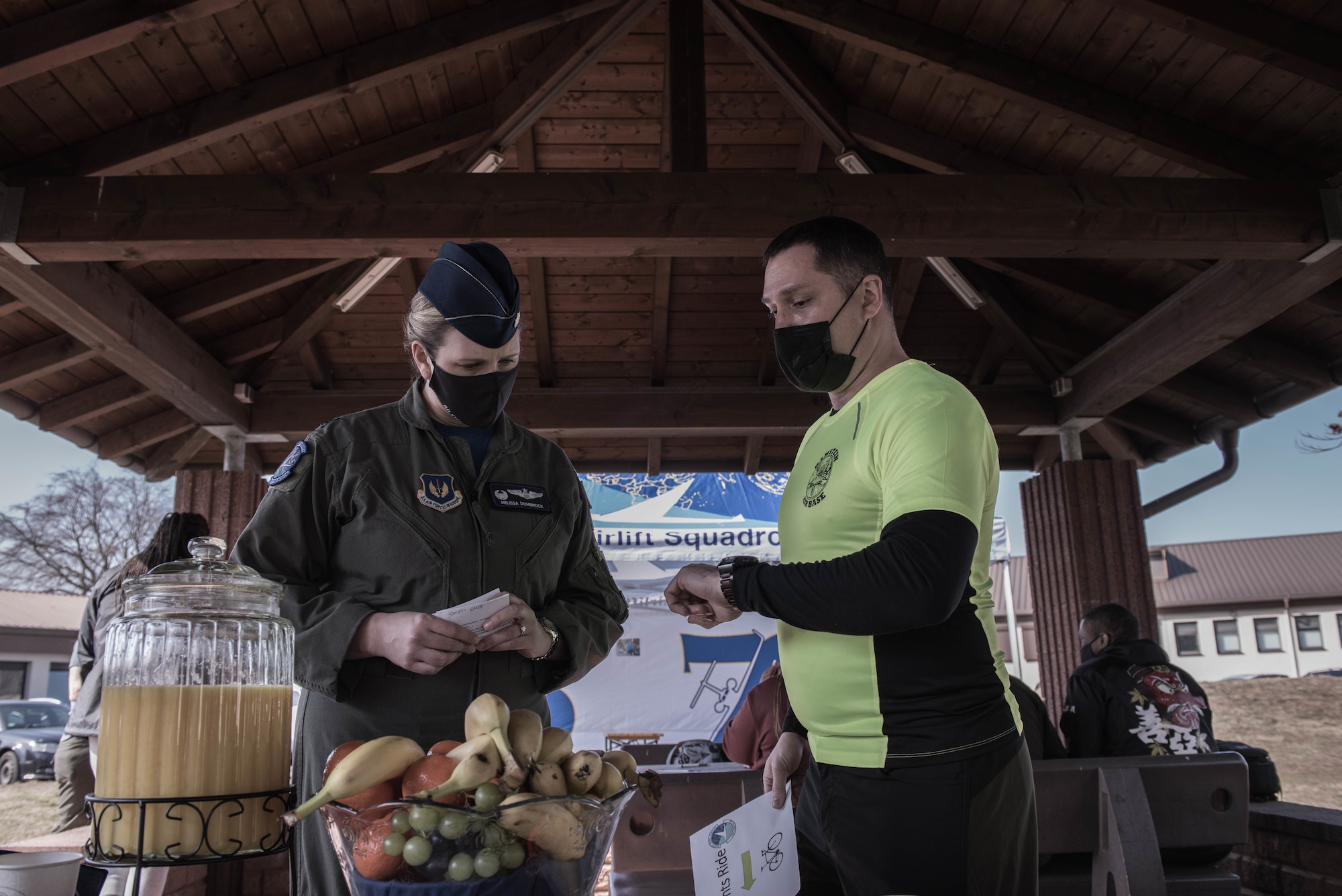 A woman and a man stand infront of fruit and juice before a memorial bicycle ride.