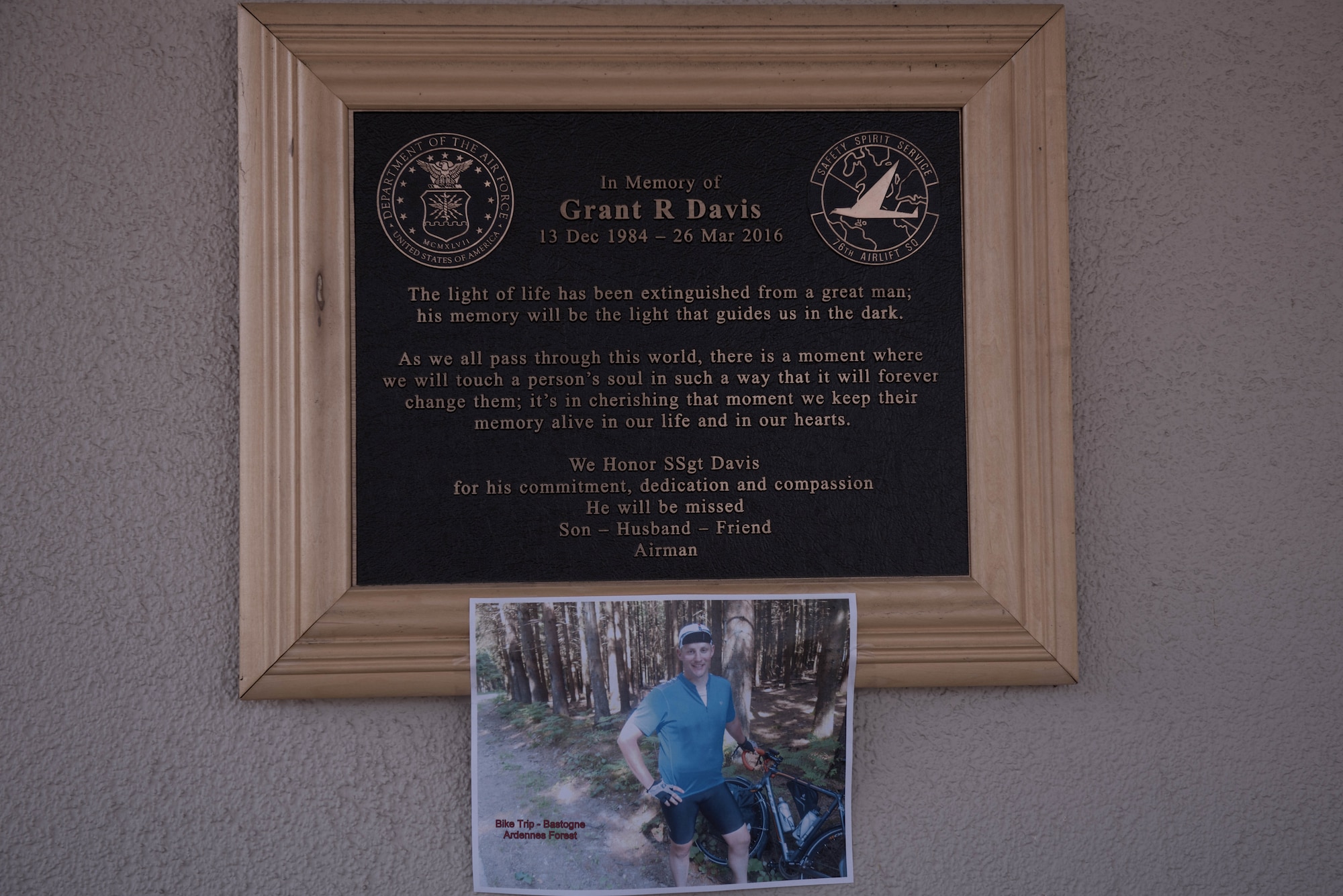 Picture of a man on a bike below a memorial plaque.