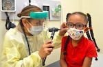 A pediatric nurse practitioner checks a 5-year-old child's ears.