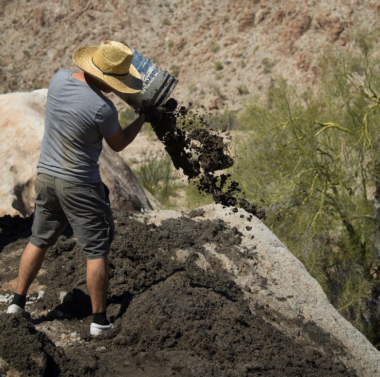 A U.S. Marine volunteer with the Single Marine Program (SMP) throws built-up silt from a Bighorn Sheep watering hole at the Betty Lee Tank in Yuma, Ariz., Mar 20, 2021. The SMP sends volunteers to help with community efforts and build relations between the community and the Marine Corps. (U.S. Marine Corps photo by Lance Cpl. Matthew Romonoyske-Bean)