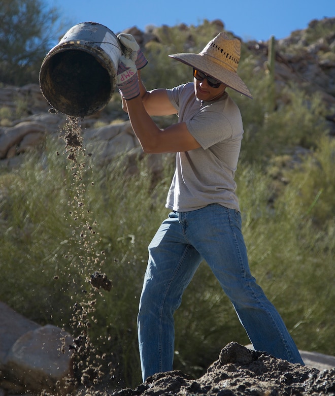 A U.S. Marine volunteer with the Single Marine Program (SMP) throws built-up silt from a Bighorn Sheep watering hole at the Betty Lee Tank in Yuma, Ariz., Mar 20, 2021. The SMP sends volunteers to help with community efforts and build relations between the community and the Marine Corps. (U.S. Marine Corps photo by Lance Cpl. Matthew Romonoyske-Bean)