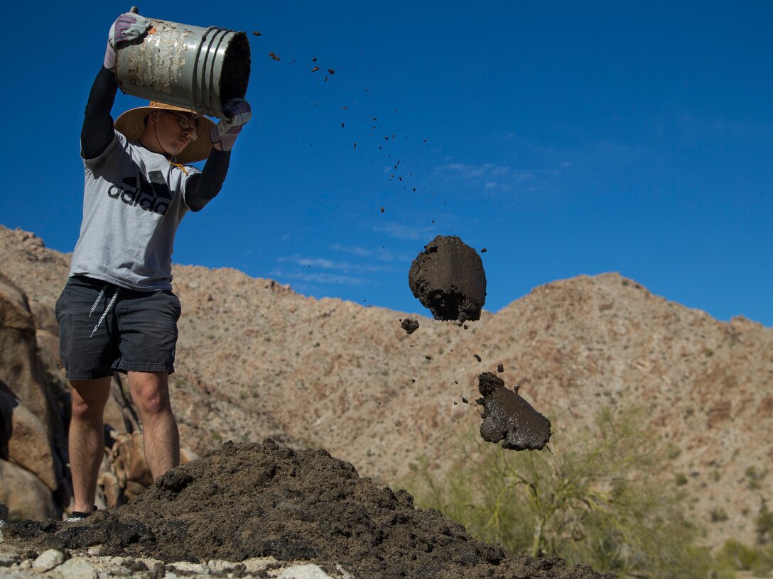 A U.S. Marine volunteer with the Single Marine Program (SMP) throws built-up silt from a Bighorn Sheep watering hole at the Betty Lee Tank in Yuma, Ariz., Mar 20, 2021. The SMP sends volunteers to help with community efforts and build relations between the community and the Marine Corps. (U.S. Marine Corps photo by Lance Cpl. Matthew Romonoyske-Bean)