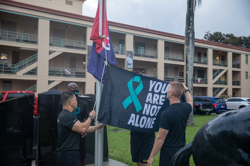 Two men place a flag on a flagpole. Another man watches.