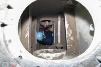 A SurgeMain (Surge Maintenance) Sailor crawling down a mock up confined space to work towards completing his required training to work with the Navy Competent Persons (NCP)—the core team responsible for confined and enclosed space safety and hot work authorization.