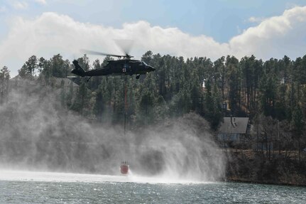 A South Dakota National Guard HH-60 Black Hawk helicopter dips a water bucket into Canyon Lake to help fight Schroeder’s Fire in Rapid City, S.D., March 30, 2021. Several dozen South Dakota National Guard members supported local, state and federal agencies to help extinguish the fire.