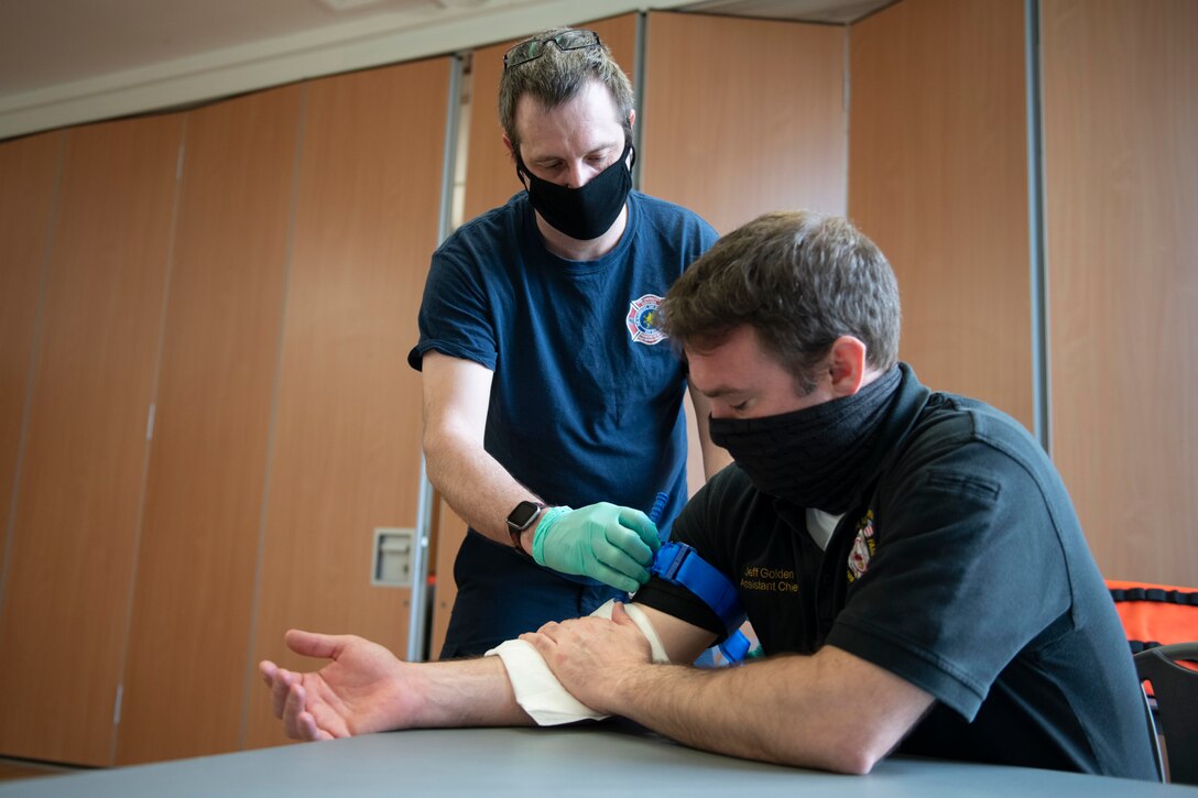 Andrew Boughen, left, 423rd Civil Engineer Squadron firefighter, binds a tourniquet on a simulated patient during an EMT practical application exam at Royal Air Force Croughton, England, March 31, 2021. U.K. firefighters across the 501st Combat Support Wing were tested in a practical application of their knowledge and skills, after attending over 280 hours of the U.S. National Registry of Emergency Medical Technicians course. The primary mission of the course was to prepare the fire department to respond to medical emergencies, as EMTs assume the responsibility of operating the ambulances and transporting patients to medical facilities. (U.S. Air Force photo by Senior Airman Jennifer Zima)