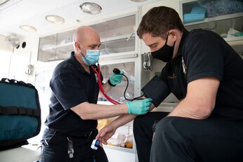 Phil Semper, left, 422nd Civil Engineer Squadron driver operator, checks blood pressure on a simulated patient with ventilation during an EMT practical application exam at Royal Air Force Croughton, England, March 31, 2021. U.K. firefighters across the 501st Combat Support Wing were tested in a practical application of their knowledge and skills, after attending over 280 hours of the U.S. National Registry of Emergency Medical Technicians course. The primary mission of the course was to prepare the fire department to respond to medical emergencies, as EMTs assume the responsibility of operating the ambulances and transporting patients to medical facilities. (U.S. Air Force photo by Senior Airman Jennifer Zima)