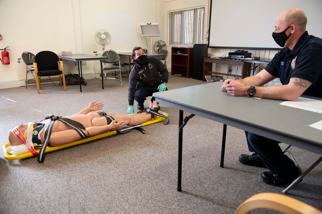 Gregg Metheringham, left, 422nd Civil Engineer Squadron firefighter driver operator, stabilizes a simulated patient to a backboard during an EMT practical application exam at Royal Air Force Croughton, England, March 31, 2021. U.K. firefighters across the 501st Combat Support Wing were tested in a practical application of their knowledge and skills, after attending over 280 hours of the U.S. National Registry of Emergency Medical Technicians course. The primary mission of the course was to prepare the fire department to respond to medical emergencies, as EMTs assume the responsibility of operating the ambulances and transporting patients to medical facilities. (U.S. Air Force photo by Senior Airman Jennifer Zima)
