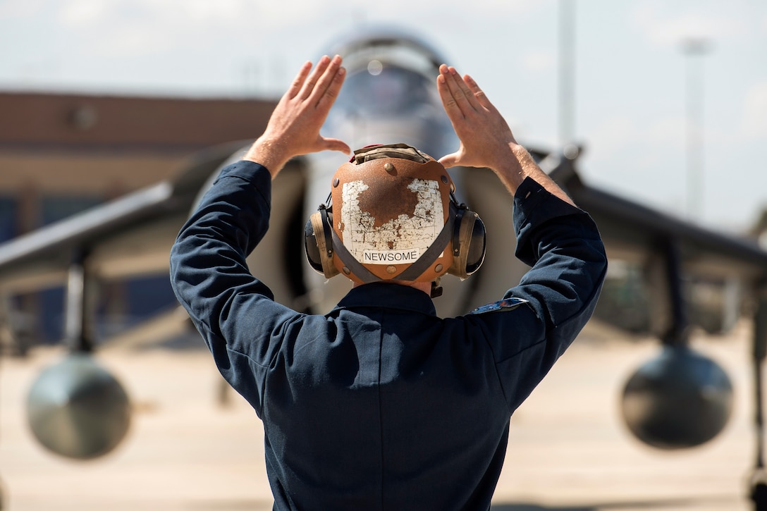 A service member signals at an aircraft.