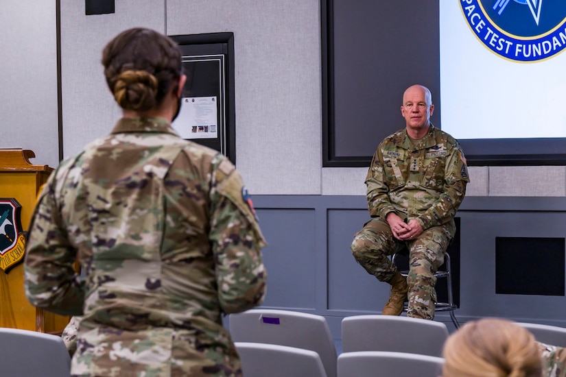 A military officer sits on a stool and answers a question from a service member.