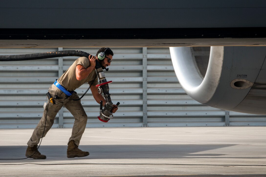 An airman carries a fuel hose next to an aircraft.