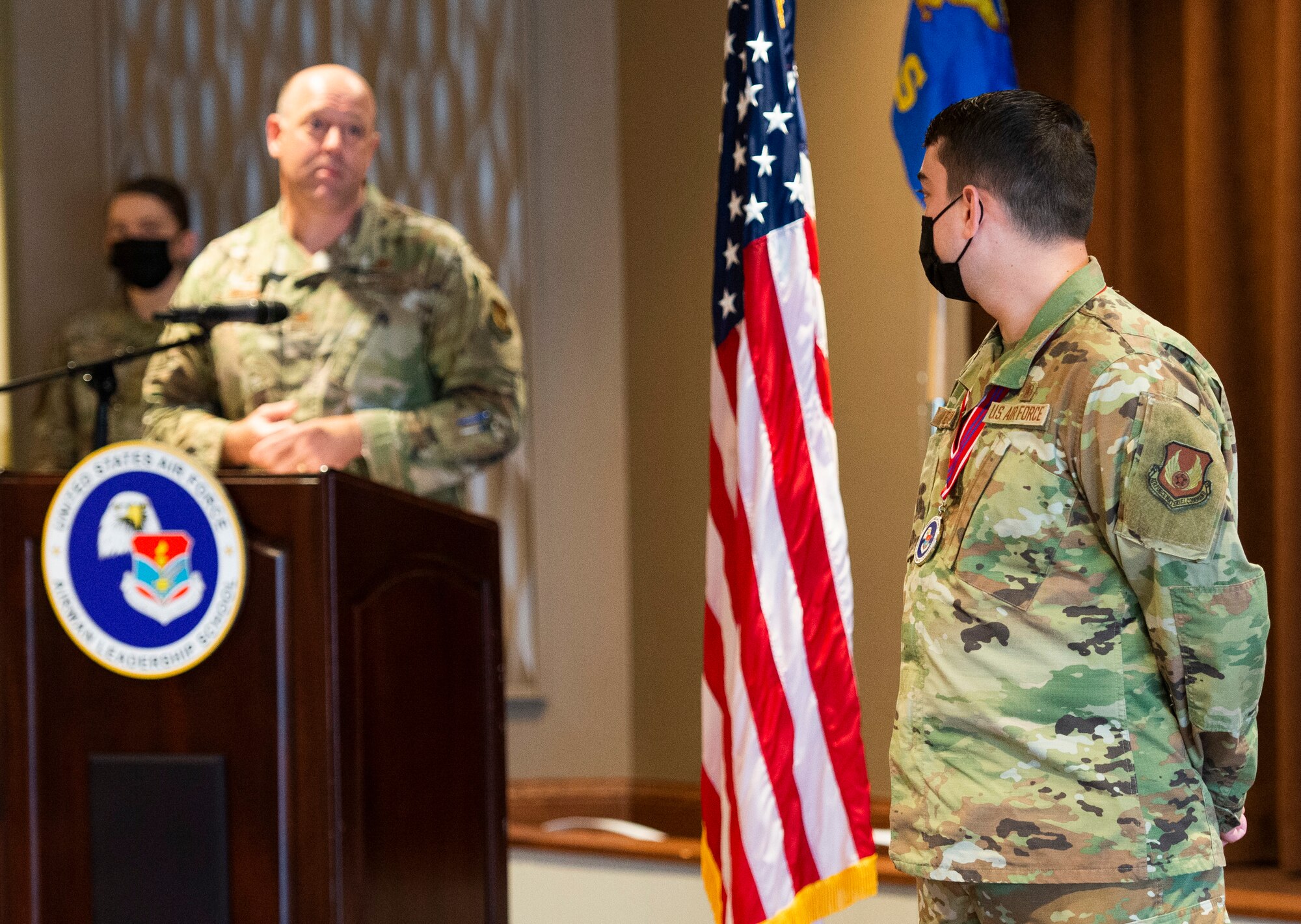 Staff Sgt. Marc Lejeune stands by while Col. Patrick Miller, 88th Air Base Wing commander, recognizes him during the Airman Leadership School Class 21-C graduation ceremony inside the base club at Wright-Patterson Air Force Base, Ohio, March 25, 2021. Miller presented a coin to Lejeune at the graduation for initiating basic first aid to a neighbor March 23. U.S. Air Force photo/Wesley Farnsworth