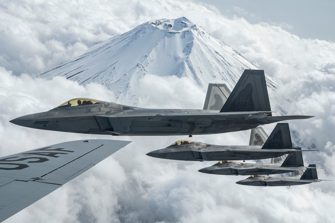 Air Force aircraft fly in a line above clouds, with Mount Fuji in the background.