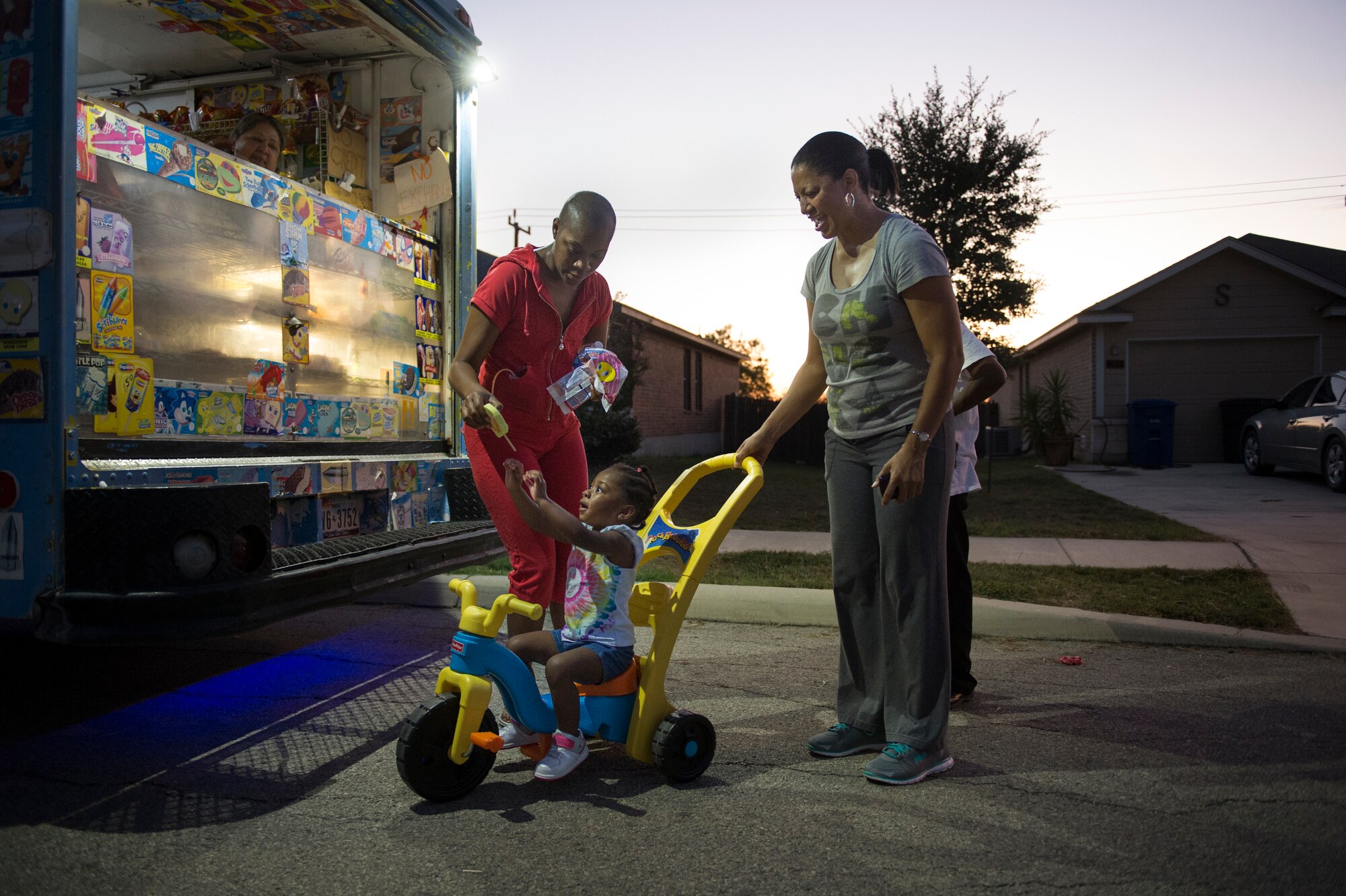 Somaya, 2, daughter of Staff Sgt. Chantel Thibeaux, Joint Base-Fort Sam Houston, Texas, dental assistant instructor, reaches up for Ice cream as her grandmother Carla guides her Big Wheel.  At two years old, Somaya is unaware of her mothers battle with cancer and tried to play with her every chance she can, but is limited to certain activities. About 15 family and friends gathered at her house to celebrate a successful surgery and provide love to Thibeaux during her quest to defeat cancer. (U.S. Air Force photo/Staff Sgt. Vernon Young Jr.)