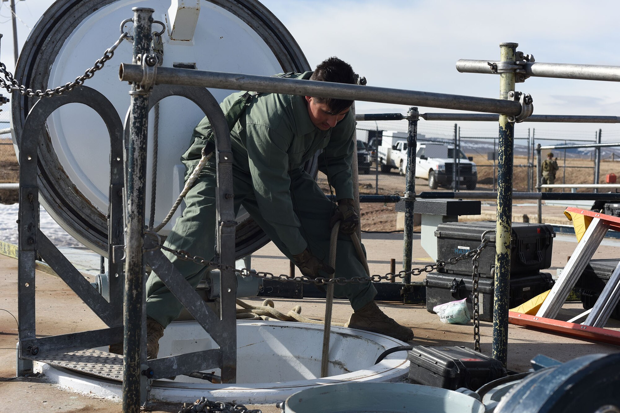 A maintainer stands above a porthole holding a hose.