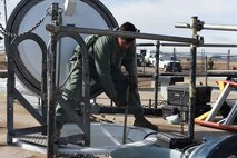 A maintainer stands above a porthole holding a hose.