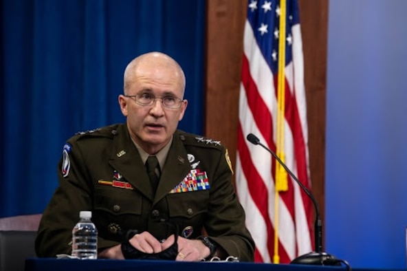 A man in an Army uniform speaks into a microphone.