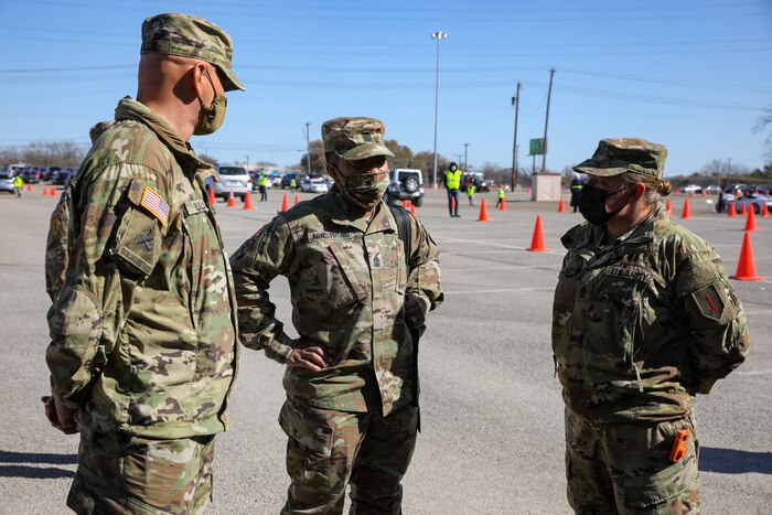 Three soldiers wearing face masks speak to each other.
