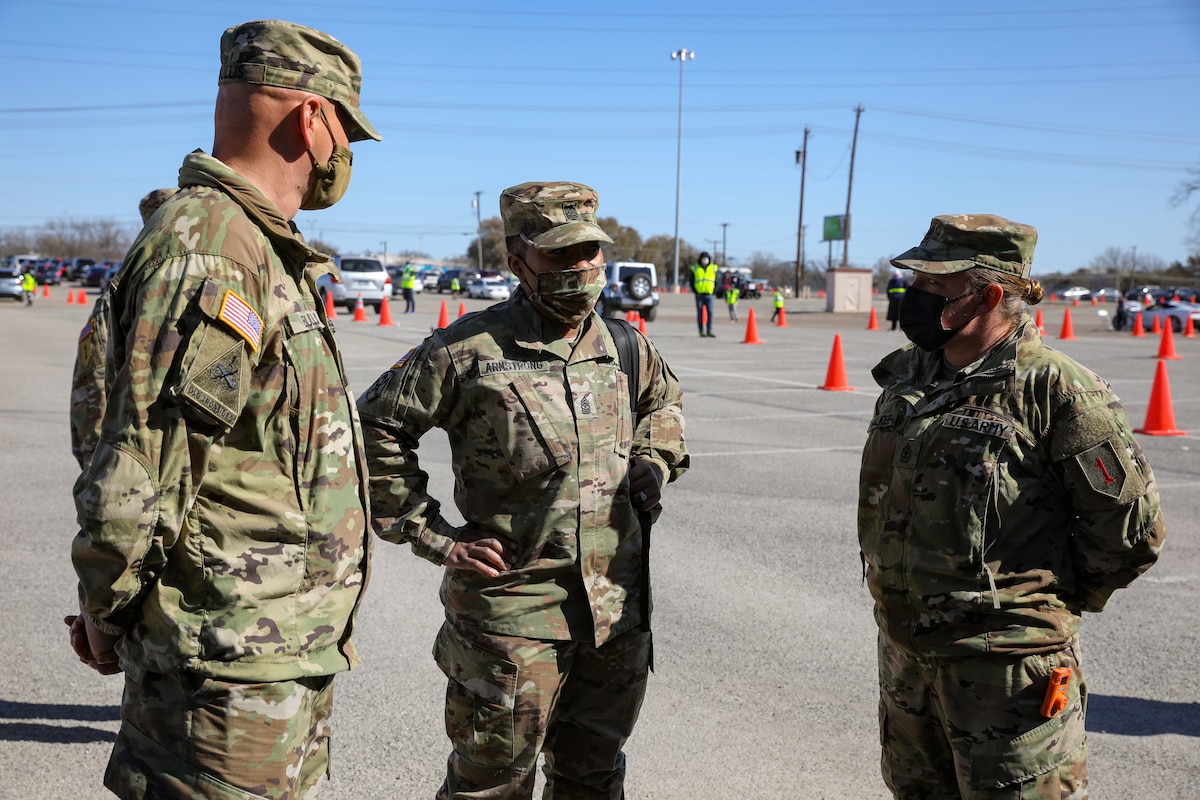Three soldiers wearing face masks speak to each other.