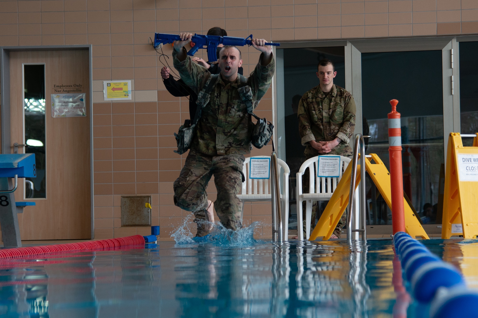 Man in uniform holding training weapon jumps in pool