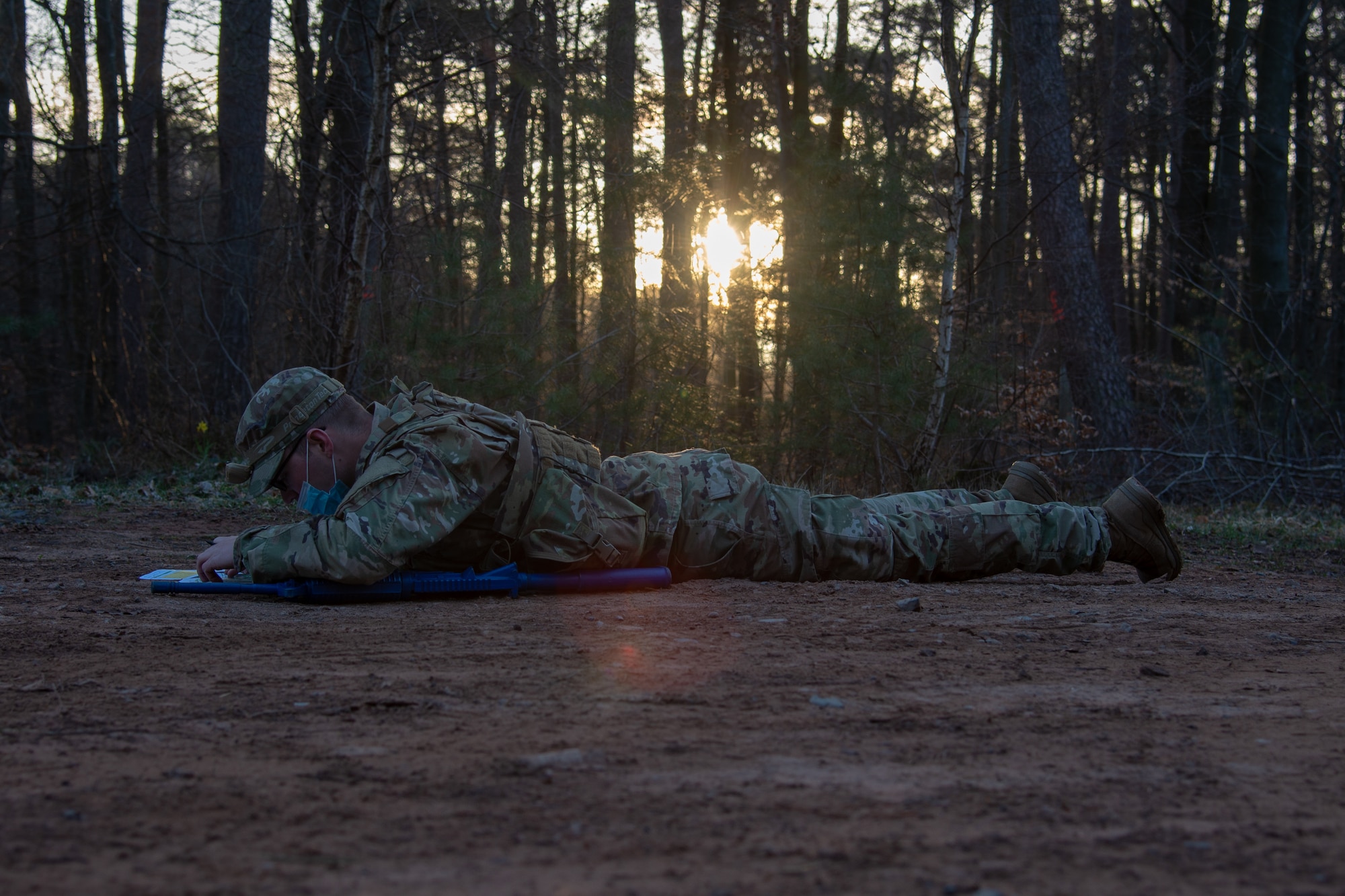 Man on his stomach in the woods reads a map