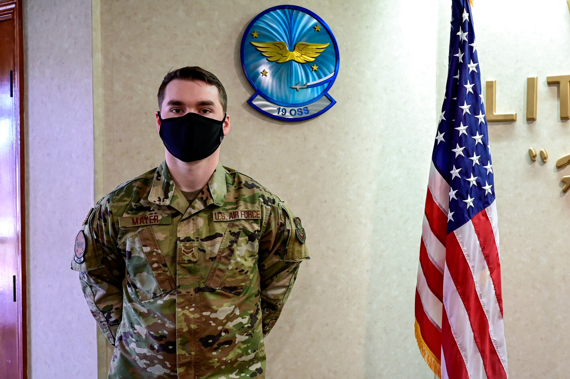 An Airman poses for a photo next to a flag.