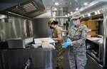 Airman 1st Class Stephany Morales, left, and Senior Airman Anna Ketchum, right, prepare food for dinner meal service during March 2021 drill weekend. The airmen prepare meals in a Disaster Relief Mobile Kitchen (U.S. Air Force Photo by Airman 1st Class Michelle Brooks).