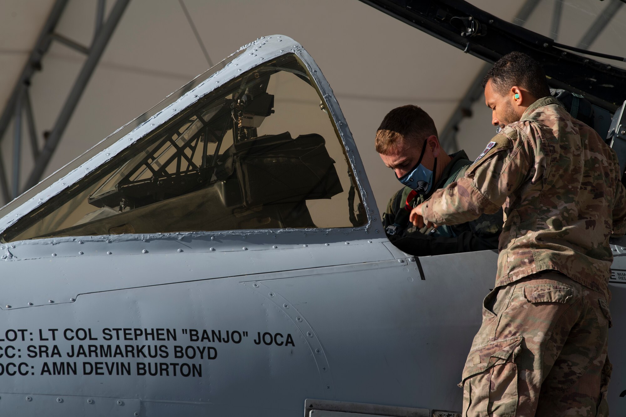 A photo of an Airman standing on a ladder outside of an A-10C Thunderbolt II, handing an object to another Airman.