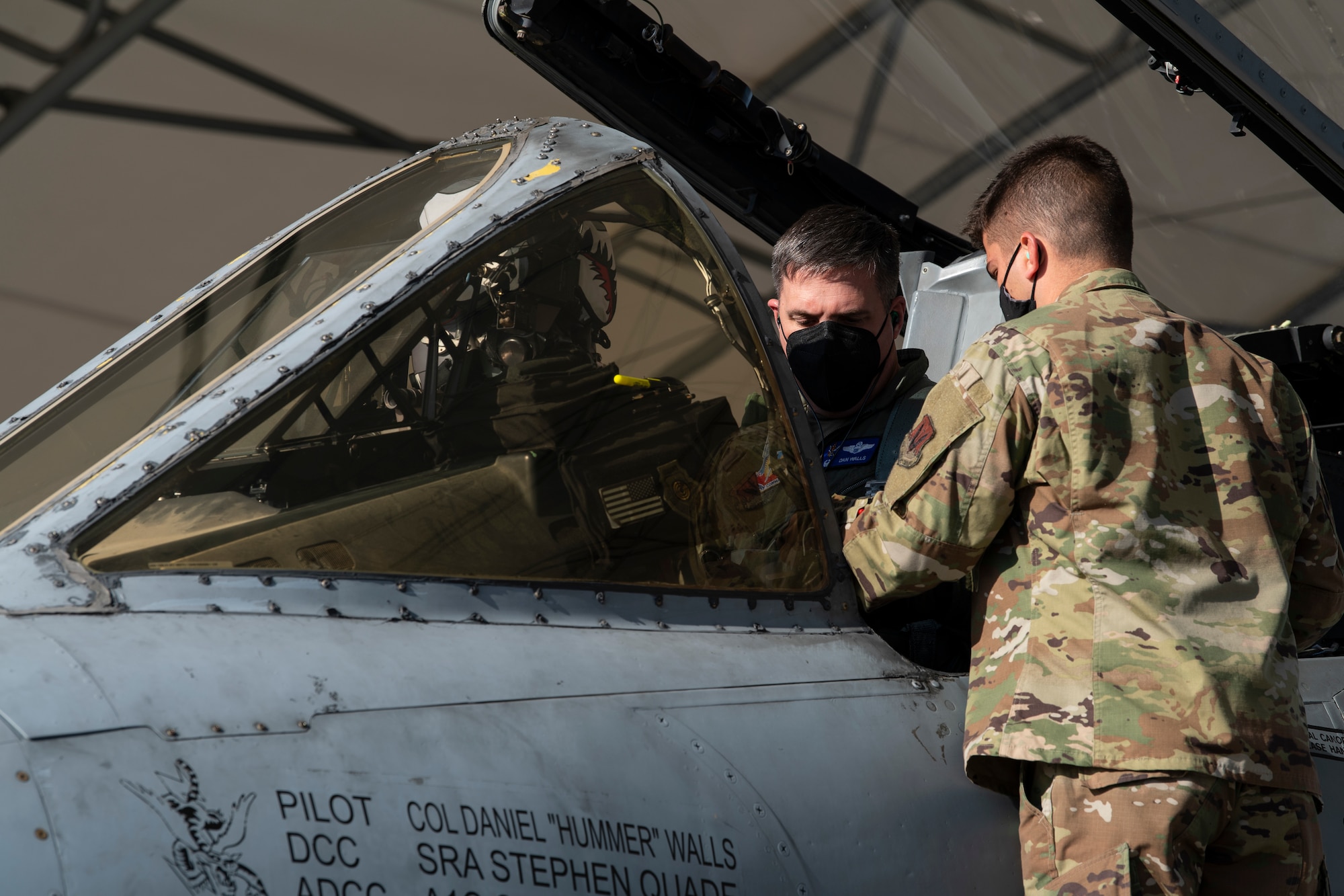 A photo of an Airman standing on a ladder outside of an A-10C Thunderbolt II, handing an object to another Airman.