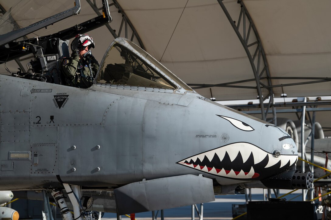 A photo of an Airman putting a helmet on, while sitting in an A-10C Thunderbolt II.