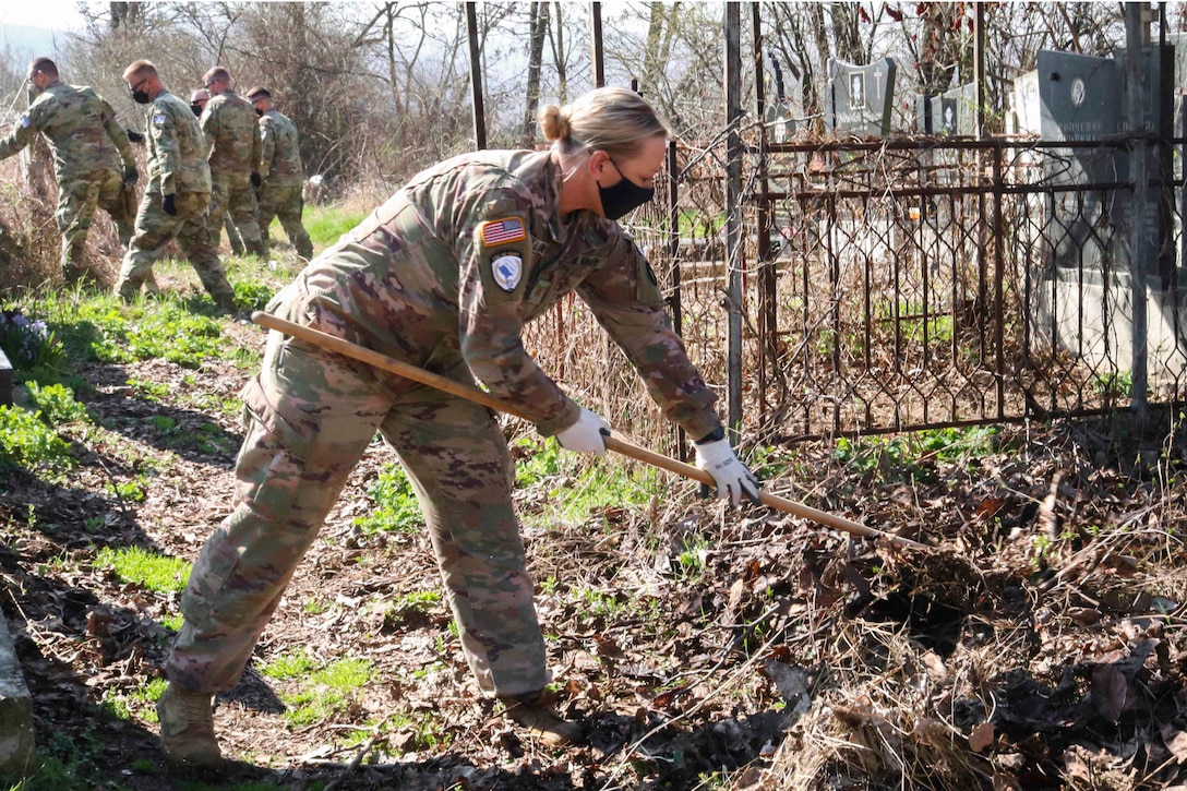 A soldier rakes weeds at a cemetery.