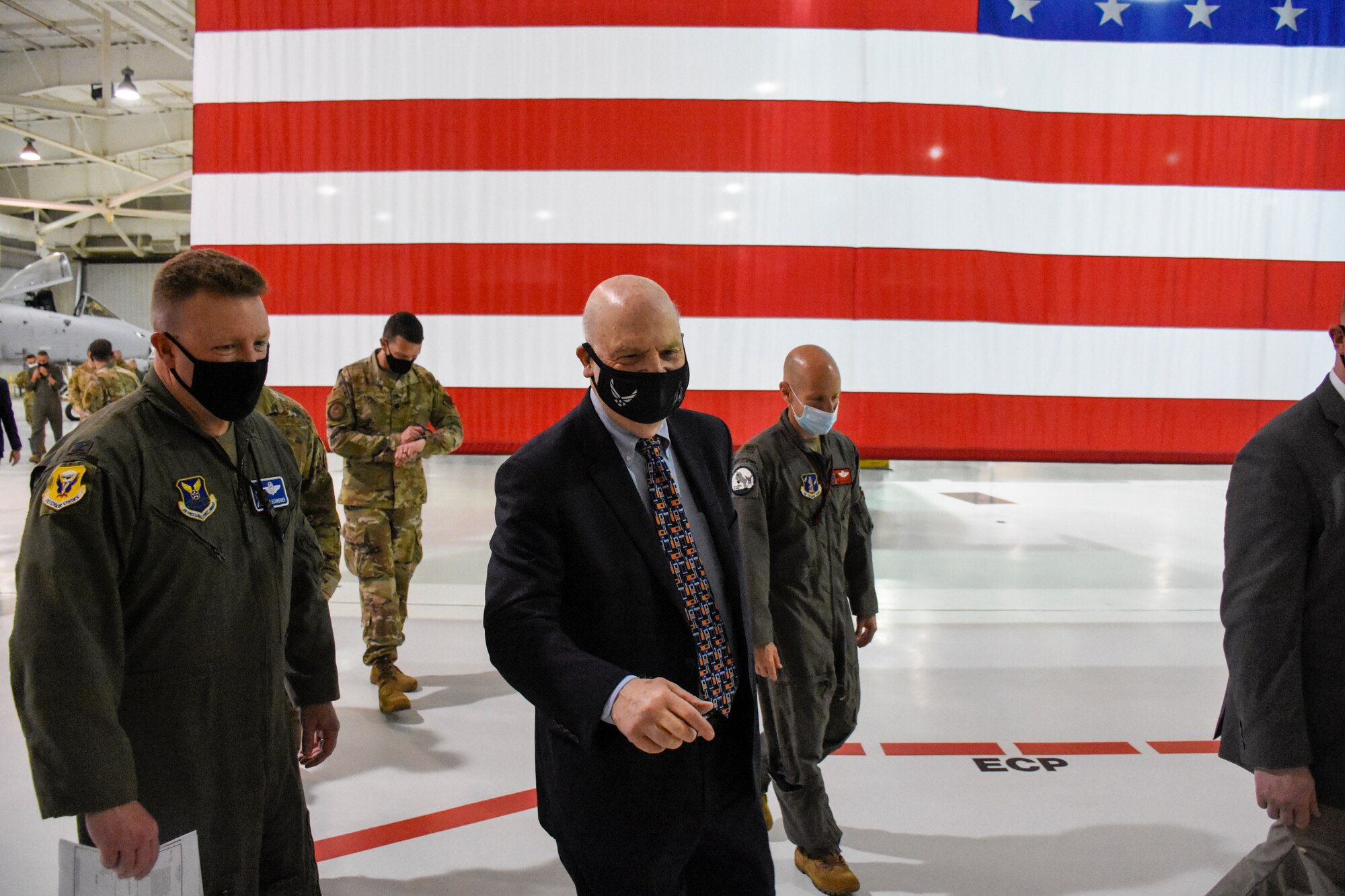 Acting Secretary of the Air Force John Roth departs the 5-Bay hangar with Colonel Jeffrey Schreiner in front of a large American flag.