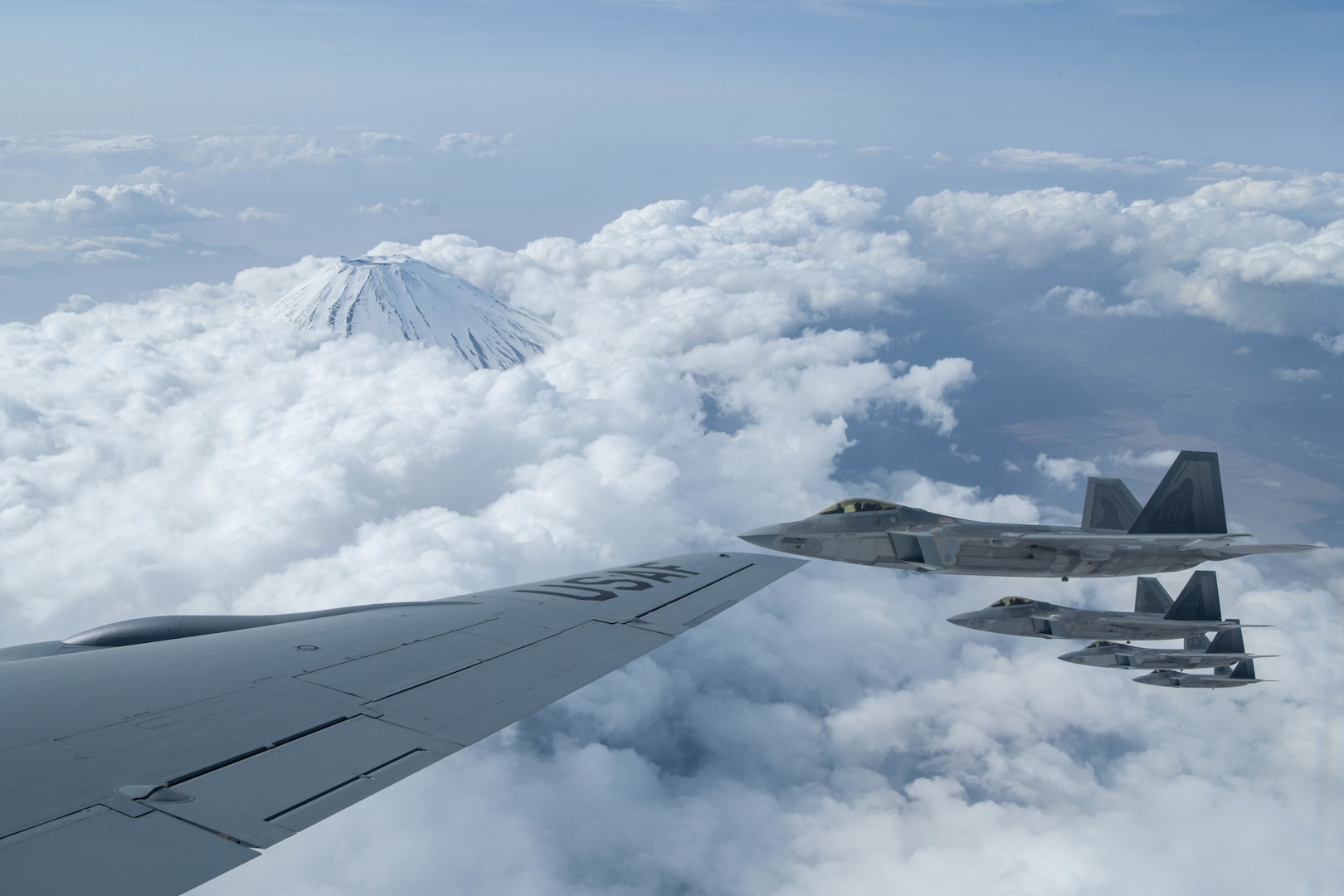 U.S Air Force Raptors from the 199th Fighter Squadron fly alongside a USAF KC-135 Stratotanker from the 909th Air Refueling Squadron during fifth-generation fighter training near Mount Fuji, Japan, April 1, 2021. The F-22 Raptors were operating out of Marine Corps Air Station Iwakuni, Japan, to support the U.S. Indo-Pacific Command’s dynamic force employment concept.