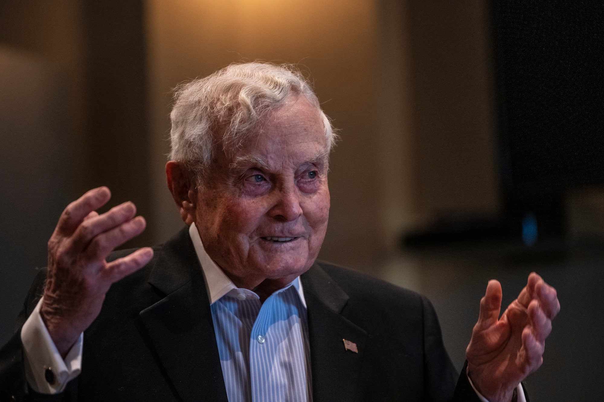 An older gentleman is making a speech and waving his arms.