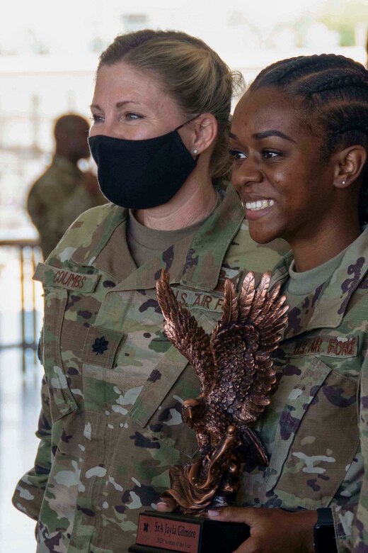 Photo of two smiling Airman posing for a photo. One is holding a large trophy.