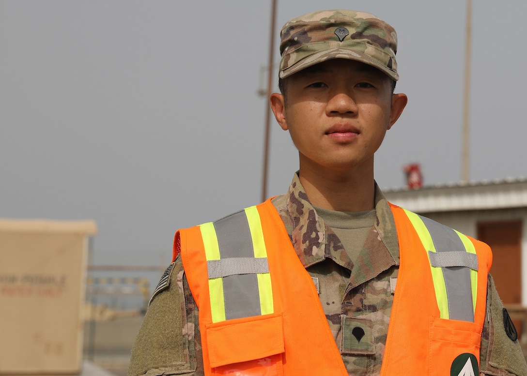 Army Reserve Spc. Feiyu He, a yard specialist deployed to Camp Arifjan, Kuwait, with the Lancaster, Pennsylvania-based 1185th Deployment and Distribution Support Battalion, stands in one of the yards his battalion operates at Kuwait's Shuaiba Port. The Chinese-born He is applying for U.S. citizenship with the support of the 1st Theater Sustainment Command's operational command post at the camp. (U.S. Army photo by Staff Sgt. Neil W. McCabe)