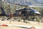 A Colorado Army National Guard Black Hawk helicopter, equipped with an aerial water bucket, departs from Button Rock Reservoir, Lyons, Colorado, to conduct bucket training in preparation for wildland fire season.