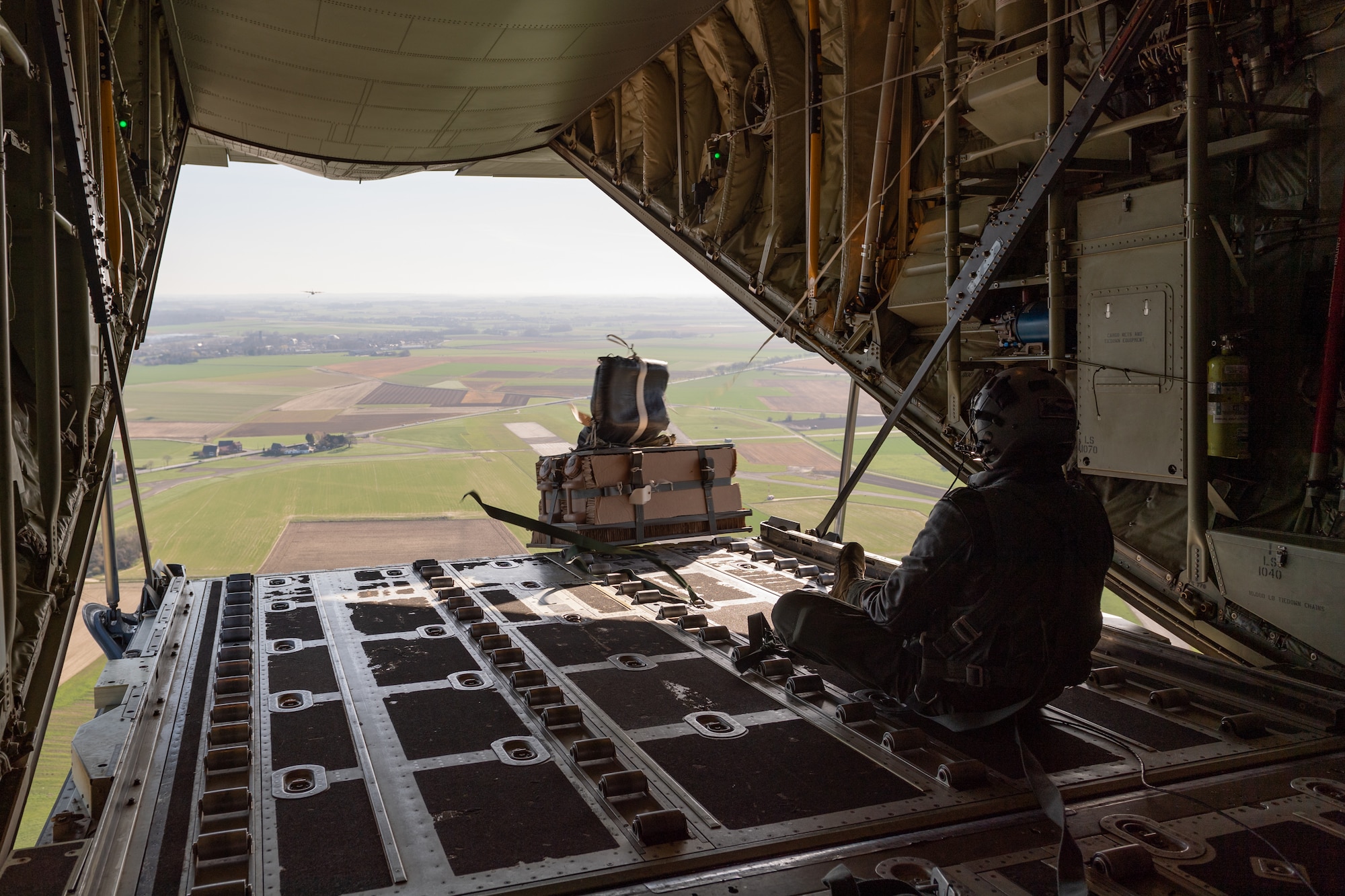 Airman sitting on an aircraft as cargo drops over edge.