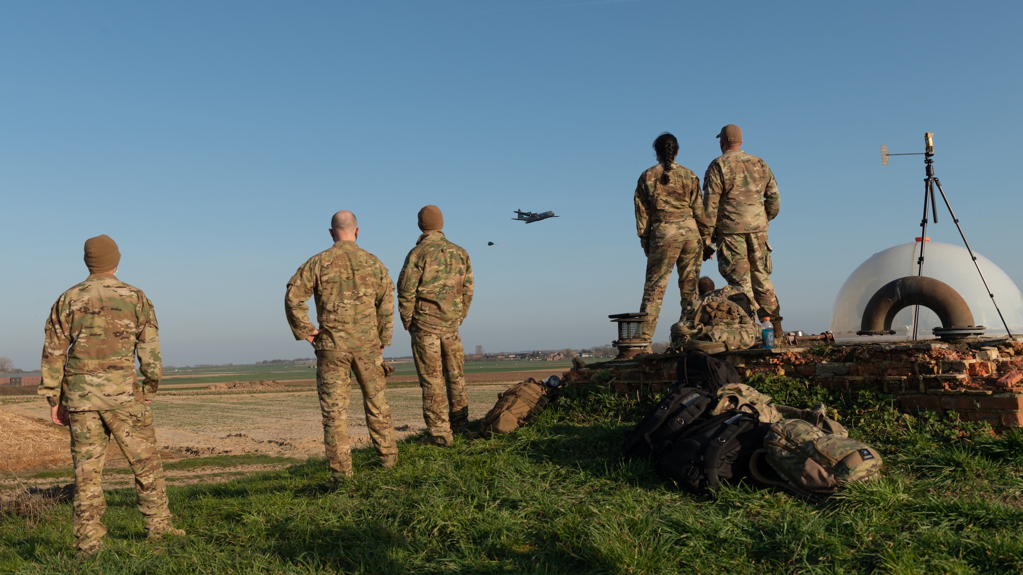 Airmen standing on a hill, looking at a plane in the distance.