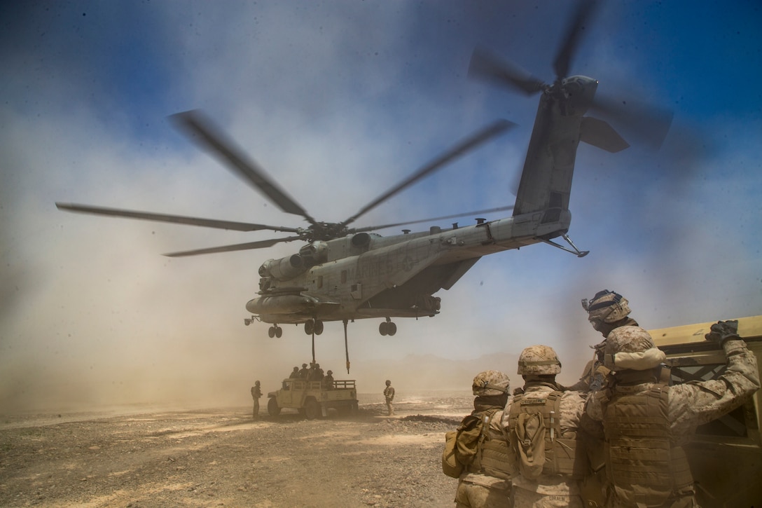 A large helicopter prepares to lift a humvee into the air.