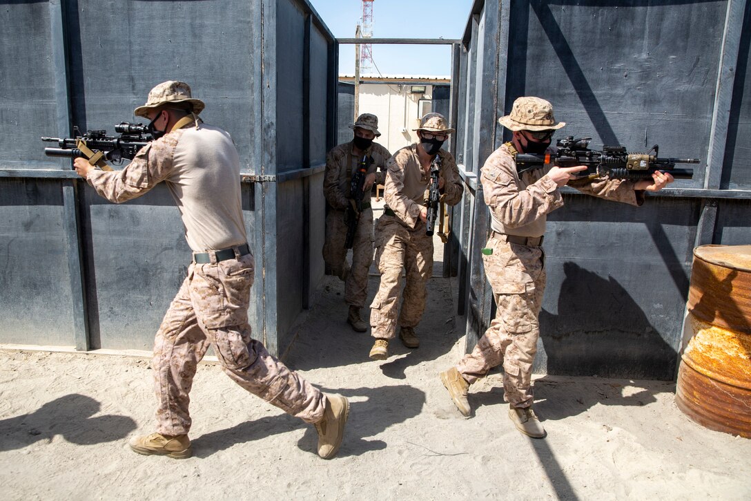 Marines run together between two buildings with guns pointed.