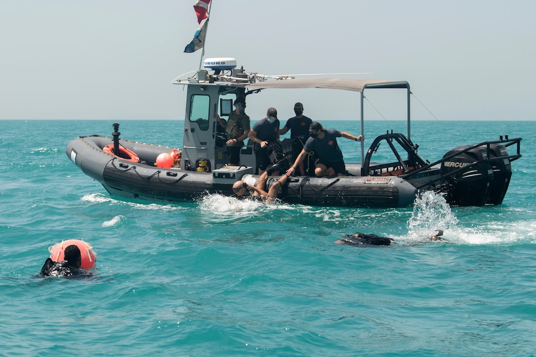 U.S. and Bahraini naval forces swim in a body of water near a small boat.