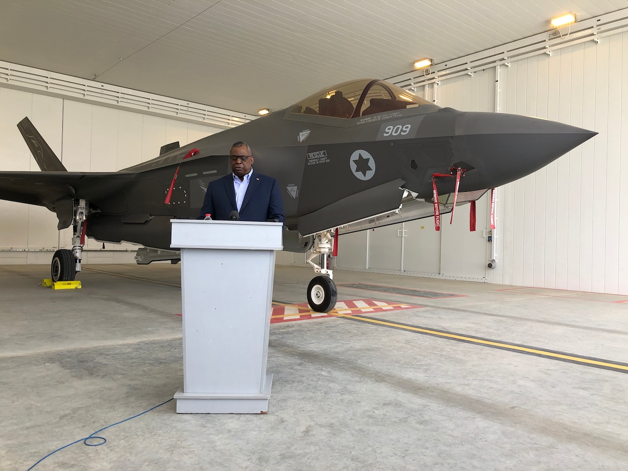 A man speaks at a podium in front of a 5th generation aircraft.