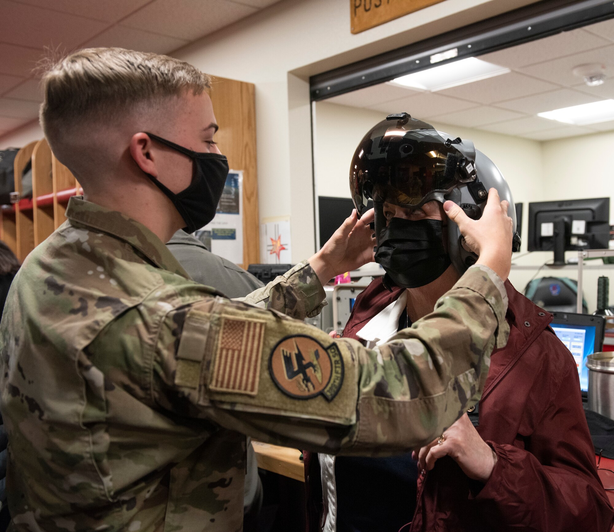 a male Airman is placing a pilots helmet onto a woman