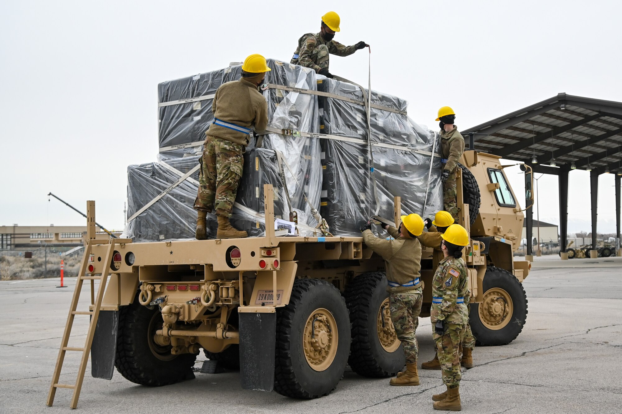 Six Airmen strapping down cargo on the bed of a military vehicle.